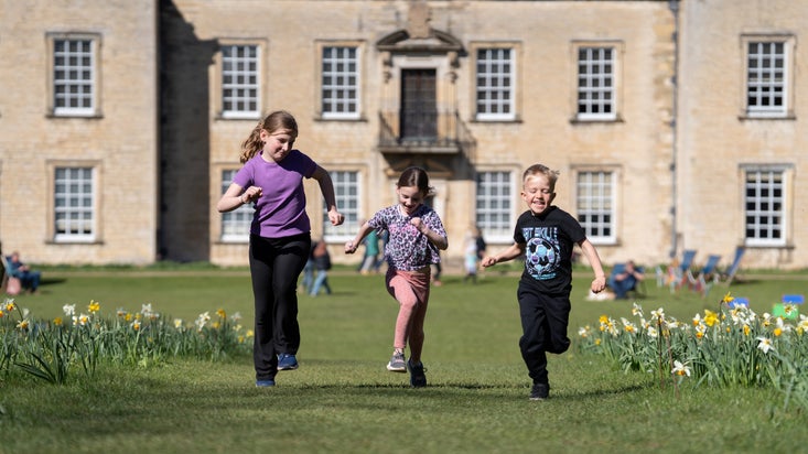 Three children running along the avenue away from the house in spring